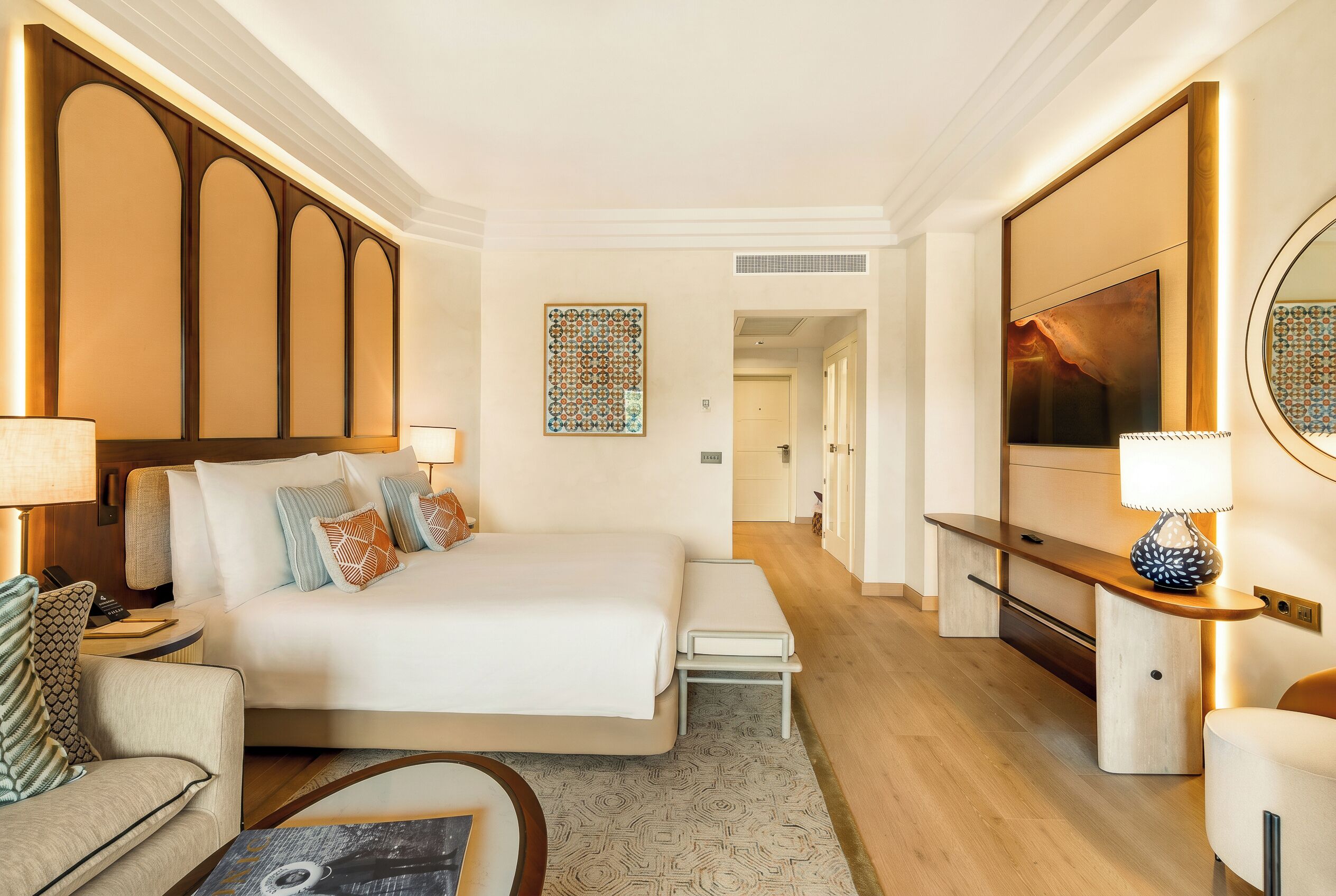 A hotel room with a bed, bedside tables, a desk, a TV, and a mirror.
