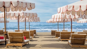 A beach with wooden lounge chairs and white umbrellas with red trim, facing the ocean. - Gran Marbella Resort & Beach Club (Marbella)