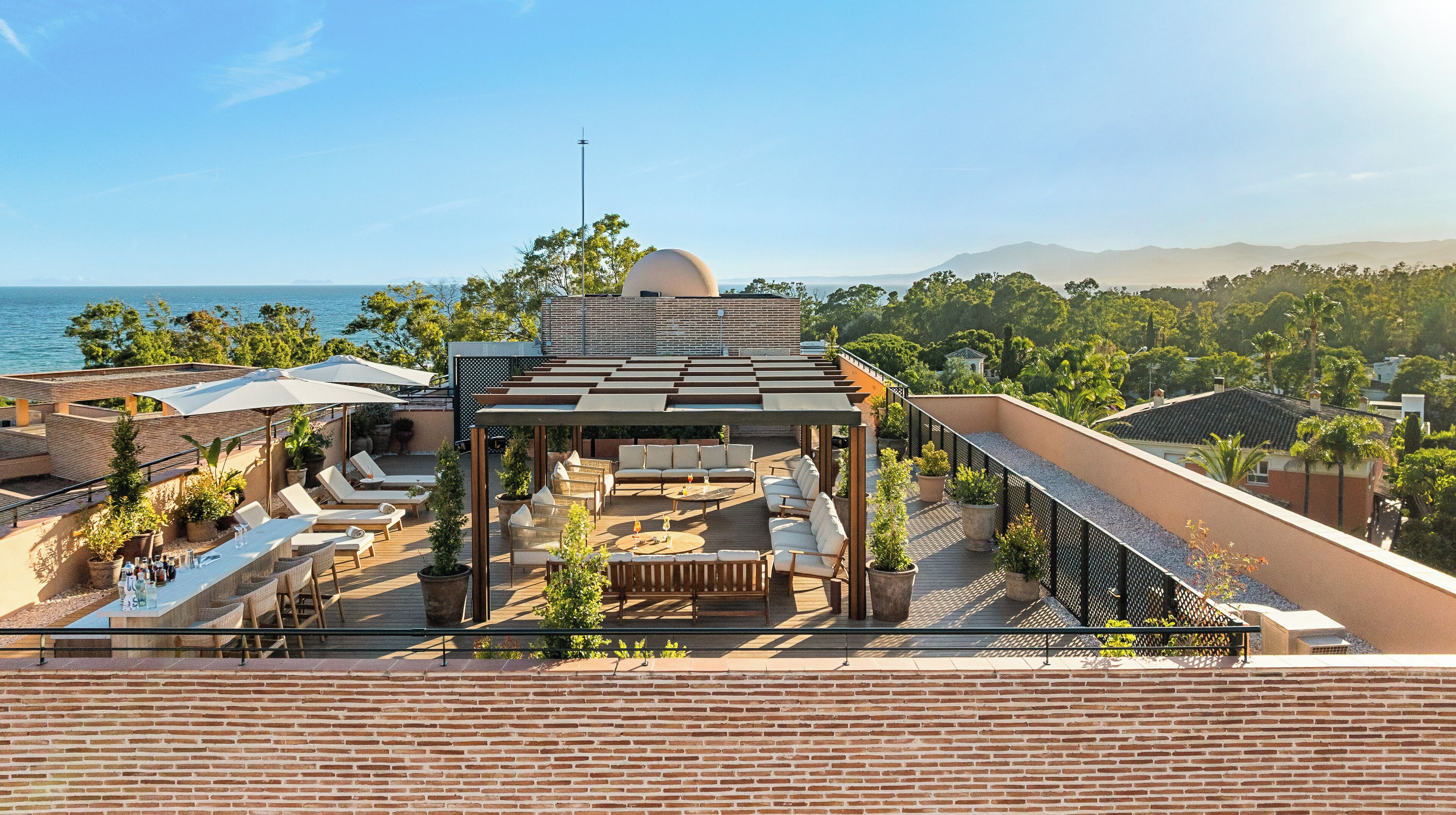 A rooftop terrace with outdoor seating, a pergola, and a view of the sea and mountains.