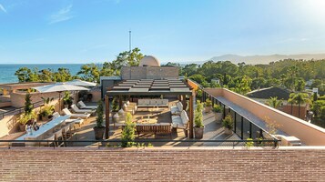 A rooftop terrace with outdoor seating, a pergola, and a view of the sea and mountains.