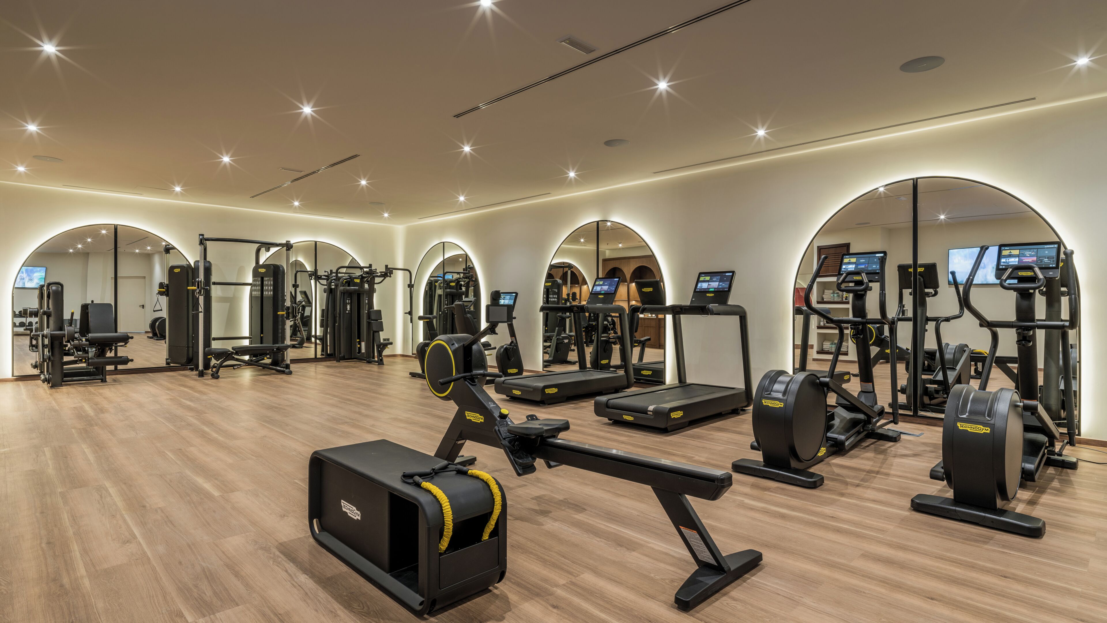 A gym with various exercise equipment, mirrored walls, and a wooden floor.