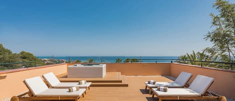 Una terraza de madera con cuatro sillas de lounge y una zona de estar integrada, con vistas a la costa.