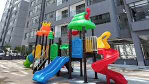 A playground with slides and climbing structures in front of a tall residential building. - Maskan Airbnbs (Nairobi)
