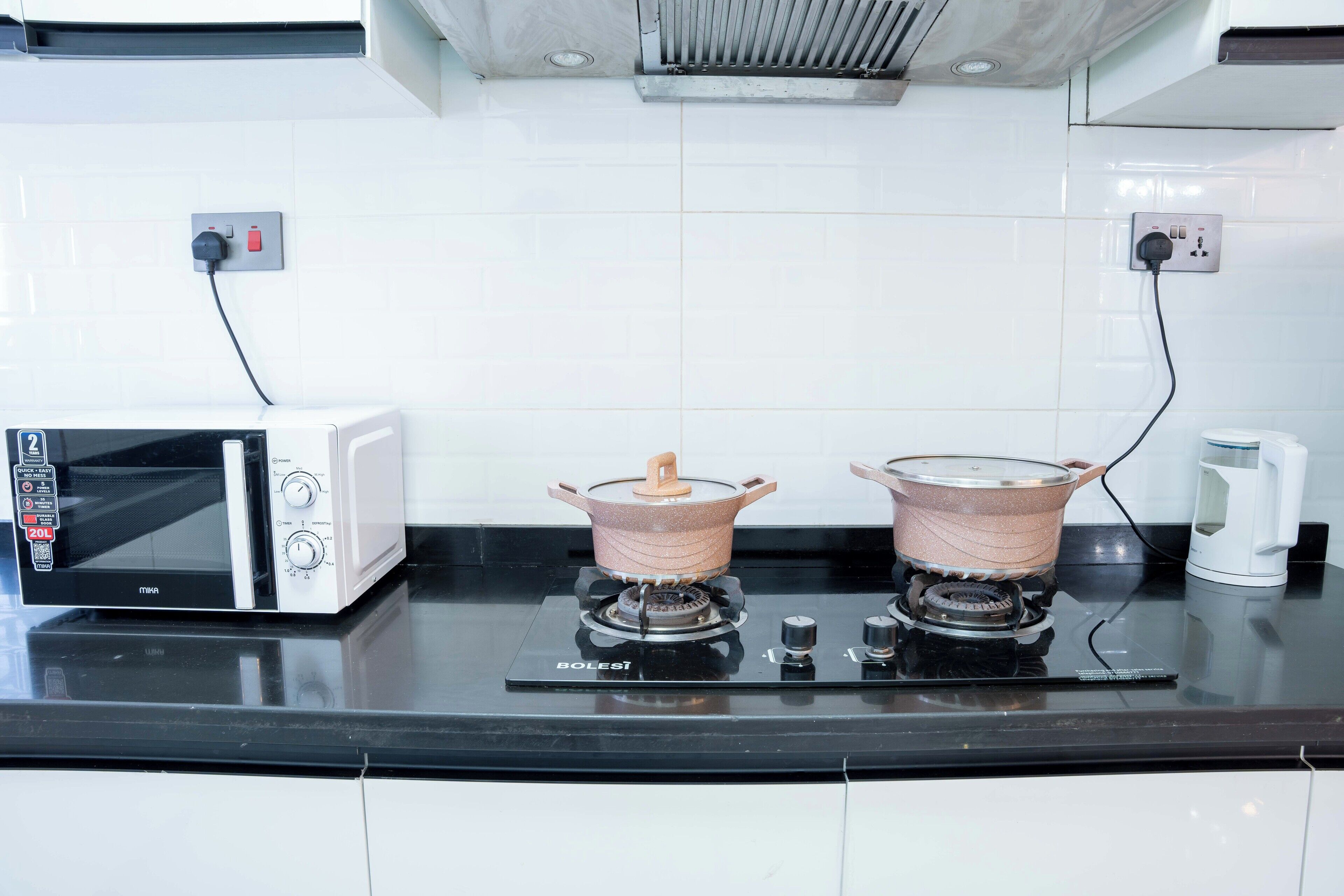 Una cocina con microondas, dos ollas sobre una estufa a gas y una cafetera.
