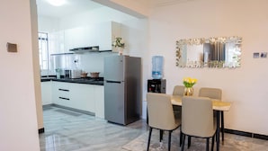 A modern kitchen with white cabinets, a stainless steel refrigerator, and a dining area with a table and chairs. - Maskan Airbnbs (Nairobi)