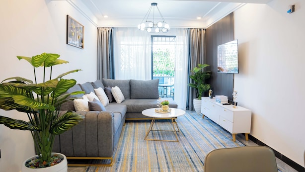 A modern living room with a grey sofa, a round coffee table, and a large potted plant. - Maskan Airbnbs (Nairobi)