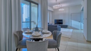 A modern living room with a dining area, large windows, and a flat-screen TV. - Cozy 1BR at Bahar with great view  (Dubai)