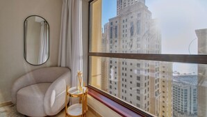 A modern room with a large window, a round mirror, a beige armchair, and a small table with a vase. - Cozy 1BR at Bahar with great view  (Dubai)
