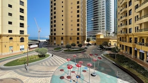 A modern residential complex with high-rise buildings, a central courtyard with red umbrellas, and a view of the sea. - Cozy 1BR at Bahar with great view  (Dubai)