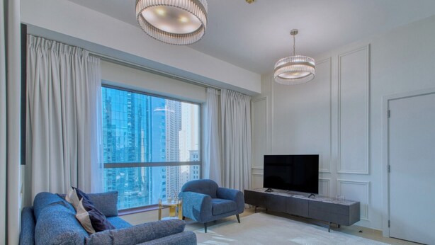 A modern living room with a large window, a flat-screen TV, a grey sofa, and a grey armchair. - Cozy 1BR at Bahar with great view  (Dubai)