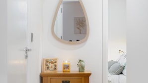 A bathroom with a wooden vanity, a mirror, a framed picture, a candle, and a small plant. - Deluxe 1 Bed Apartment, London (London)
