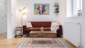 A living room with a red sofa, a coffee table, a colorful rug, a floor lamp, and a painting of an elephant. - Deluxe 1 Bed Apartment, London (London)