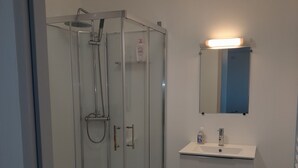 Een moderne badkamer met een douchecabine van glas, een witte wastafel met spiegel en een blauw vloerkleed.