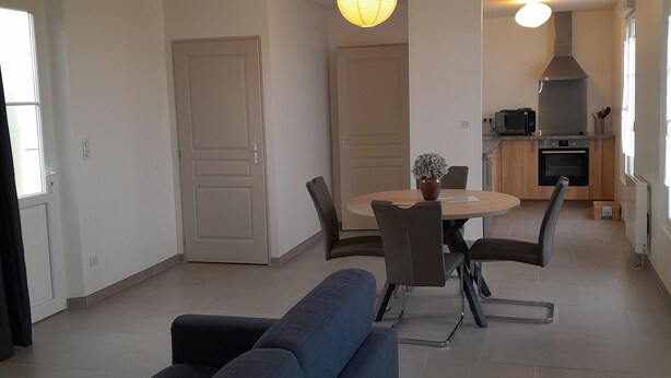 Een moderne woonkamer met een bank, een eettafel met stoelen en een keukenhoek met fornuis en oven.