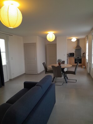 En moderne stue med sofa, spisebord med stole og et køkkenområde med komfur og ovn.