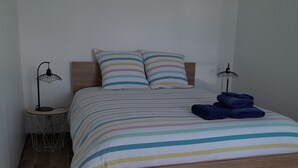 Een net opgemaakt bed met gestreept beddengoed, een houten hoofdbord en twee bedlampjes.