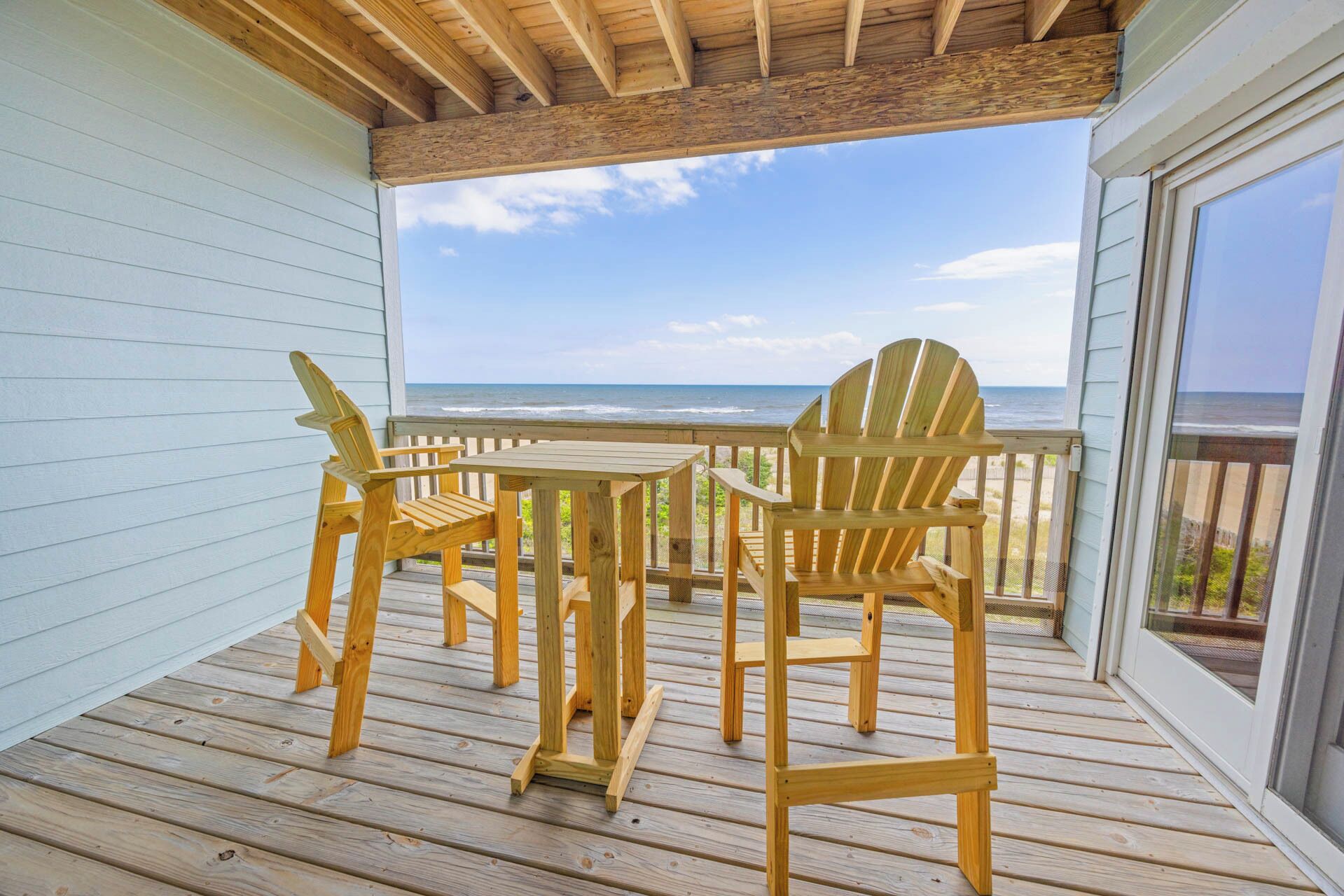 A wooden deck with a table and chairs, overlooking a beach.