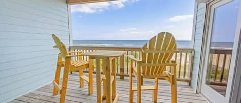 A wooden deck with a table and chairs, overlooking a beach.