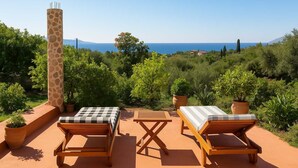 Una terraza con dos sillones de madera, una mesa a cuadros y una escultura alta de jirafa.