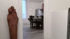 A hallway with a statue, a dining area with a table and chairs, and a kitchen area with cabinets and a refrigerator. - l'Atelier USU15 downtown Grenoble (Grenoble)