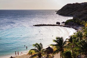 A beach with clear blue waters, a rocky outcrop, and palm trees. - Blue Bay's Tropical Art Escape (Willemstad)