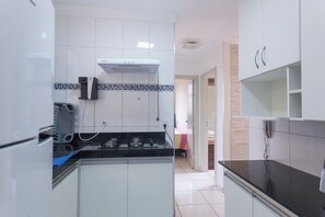 Compact kitchen with stove, wall-mounted exhaust hood, and tiled backsplash.