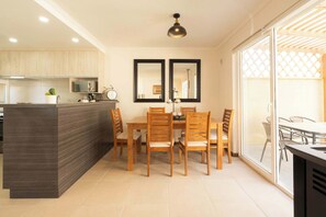 Een moderne keuken met houten kastjes, een centraal eiland en een eethoek met houten stoelen en een tafel.
