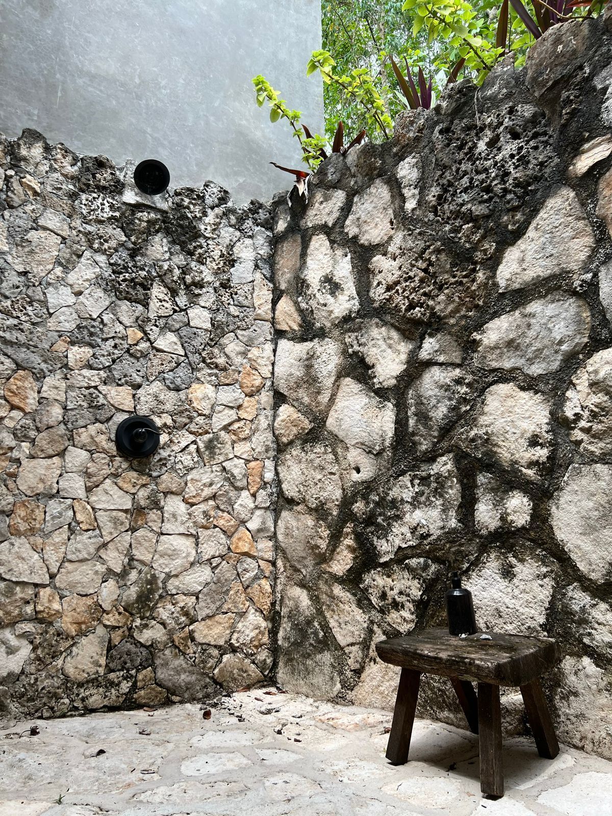 Eine steine Mauer mit einer rustikalen Bank und zwei schwarzen, runden Objekten.