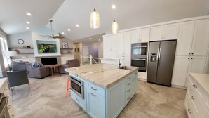 A modern kitchen with white cabinets, a marble island, stainless steel appliances, and pendant lighting.
