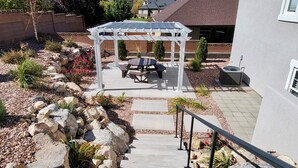 A patio area with a pergola, outdoor seating, and a stone pathway leading to a house.