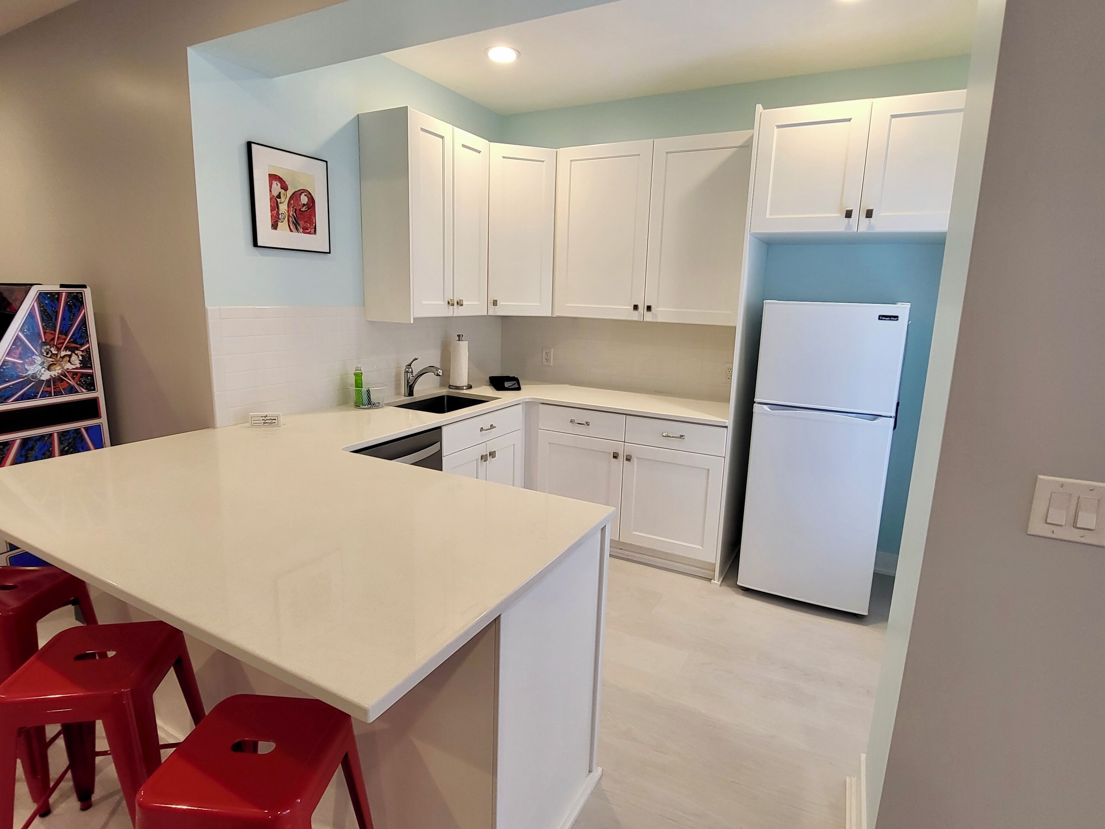 Une cuisine moderne avec des meubles blancs, un réfrigérateur blanc et un grand îlot central doté de tabourets rouges.