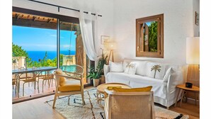 Un salon chaleureux avec un canapé blanc, un coin repas avec des chaises et une vue sur l’océan.