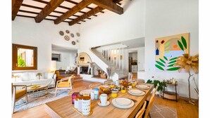 Un vaste espace dédié à la salle à manger, avec une table en bois dressée pour le petit-déjeuner, un escalier menant à l’étage supérieur et une grande peinture abstraite accrochée au mur.