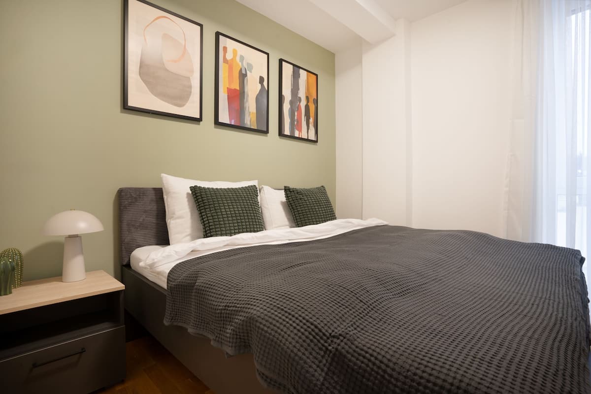 A bedroom with a bed, pillows, a nightstand, a lamp, and artwork on the wall.