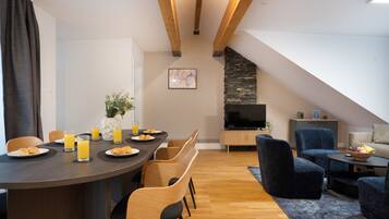 Een moderne eethoek met een houten tafel, stoelen en ontbijtartikelen. Er is een stenen open haard en een televisie op de achtergrond.