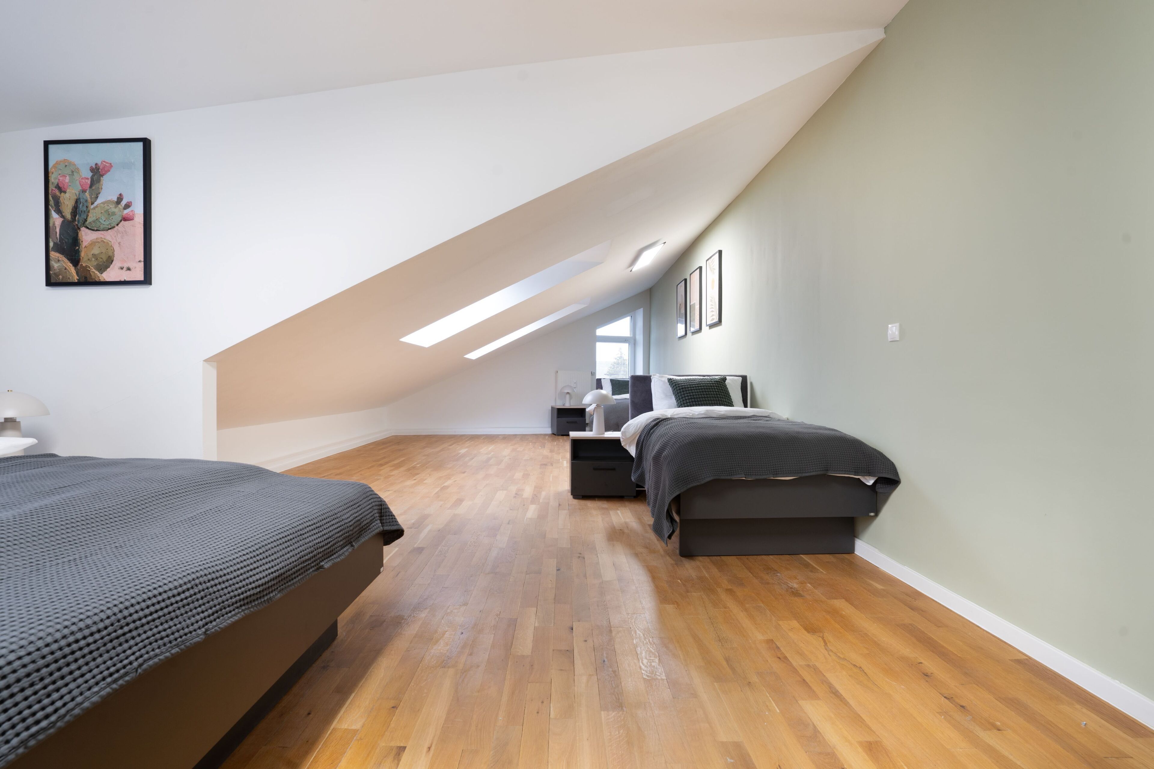 Quarto com duas camas, piso de madeira, teto inclinado e um quadro de cactos na parede.