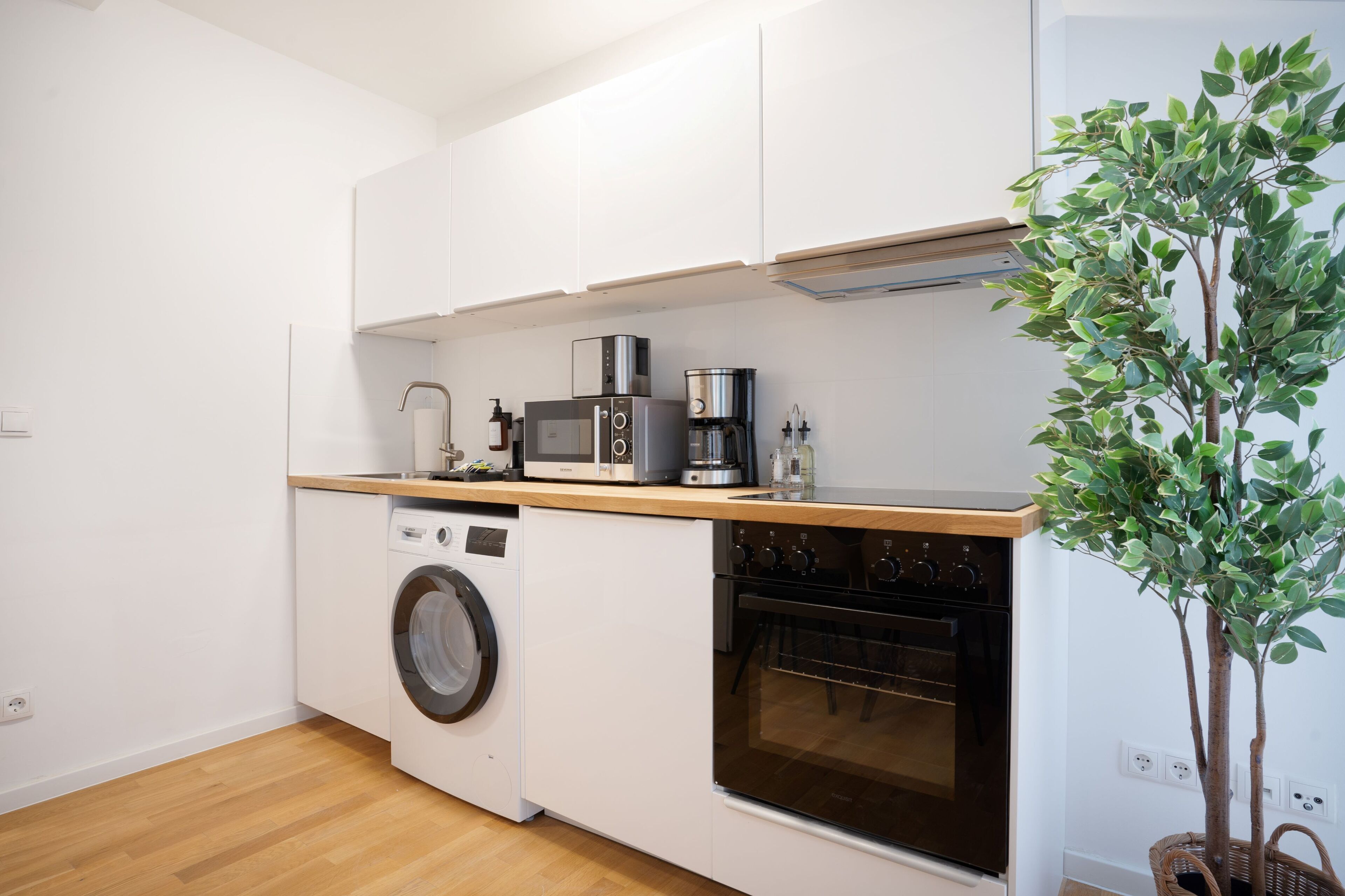 Une cuisine compacte équipée d’un lave-linge, d’un four, d’un four à micro-ondes et d’une machine à café.