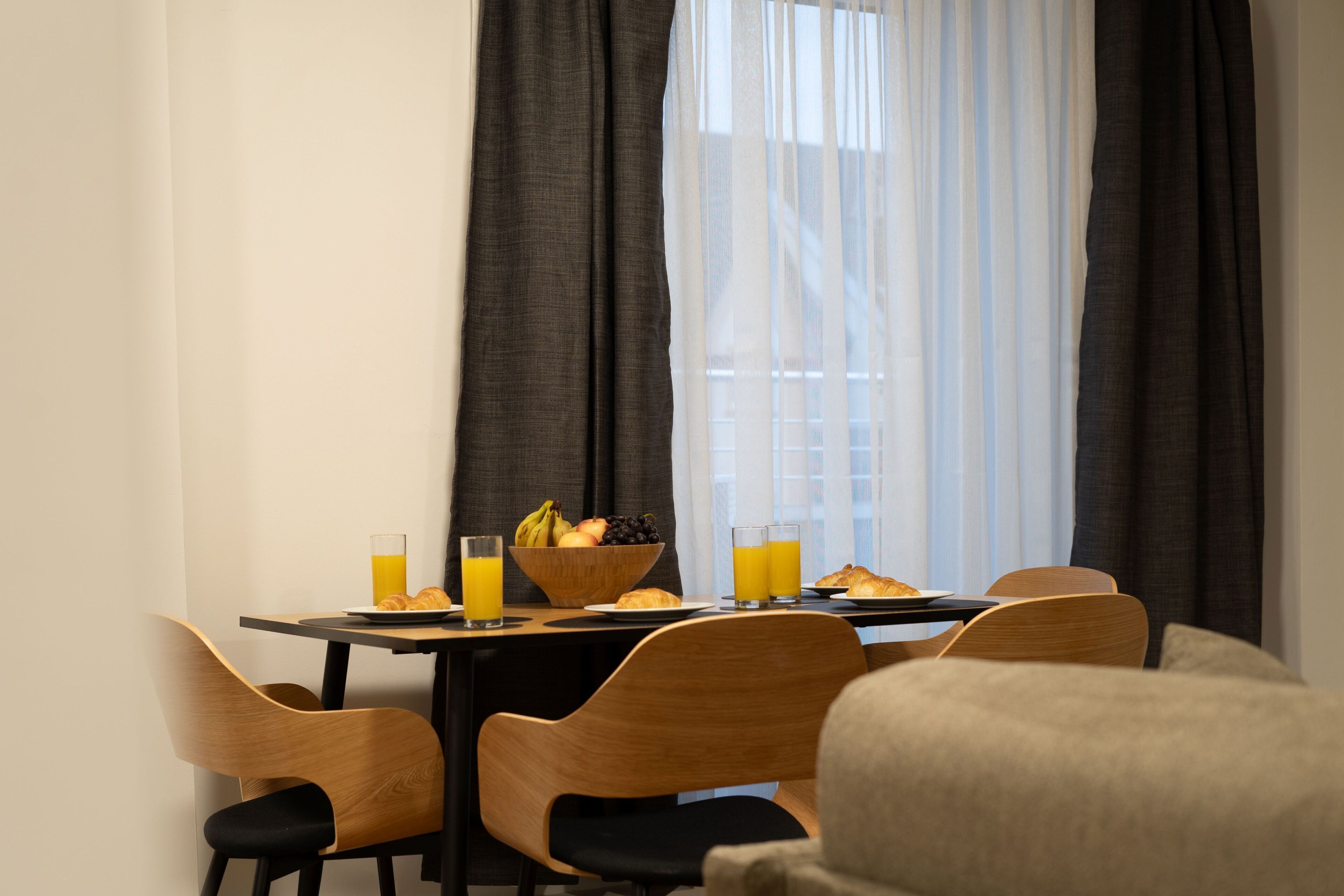 A breakfast table with a bowl of fruit, croissants, and orange juice glasses.