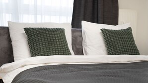 A neatly made bed with white and green pillows, a dark grey blanket, and a window with sheer curtains. - Schöne Apartments in Bad Honnef (Bad Honnef)