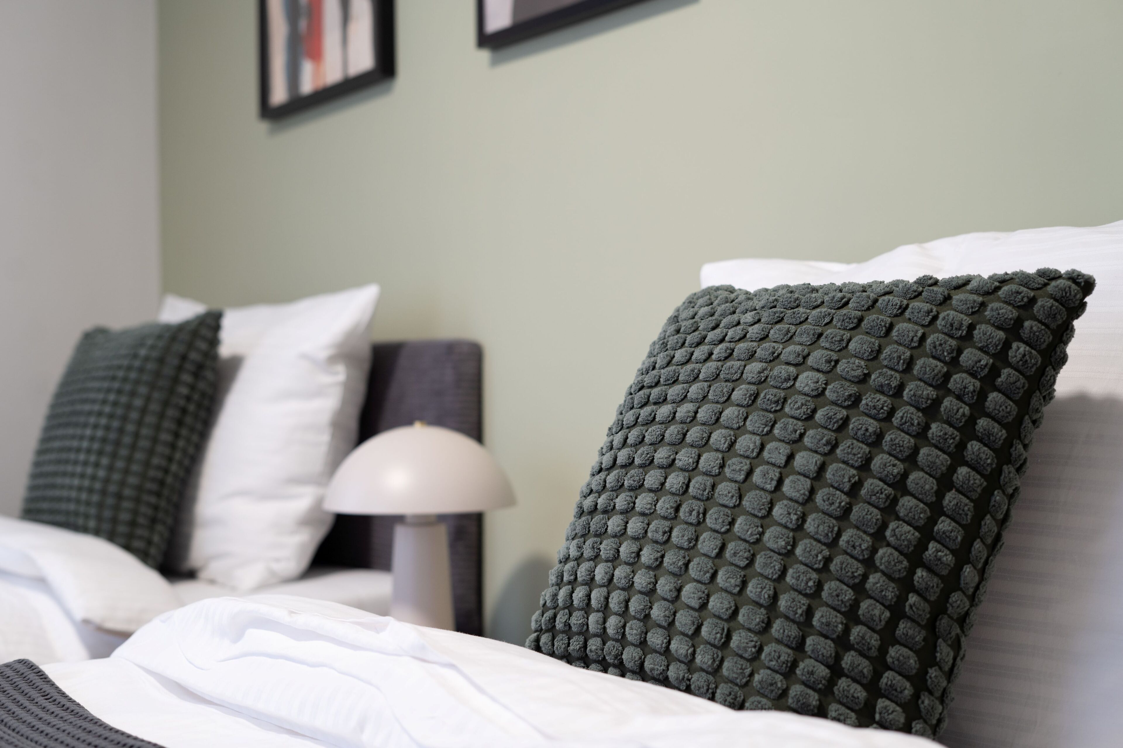 A neatly made bed with white linens and two green textured pillows.