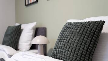 A neatly made bed with white linens and two green textured pillows.