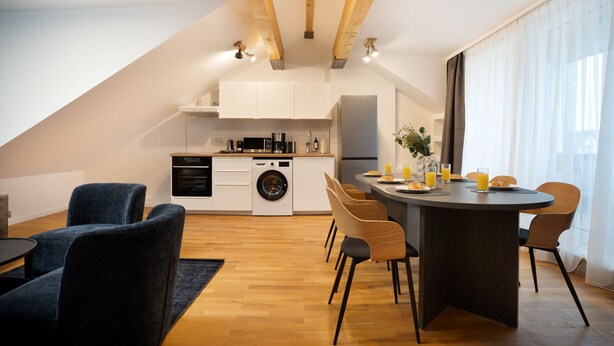A modern kitchen with white cabinets, a built-in oven, and a washing machine. There is a dining area with a round table and chairs. - Schöne Apartments in Bad Honnef (Bad Honnef)