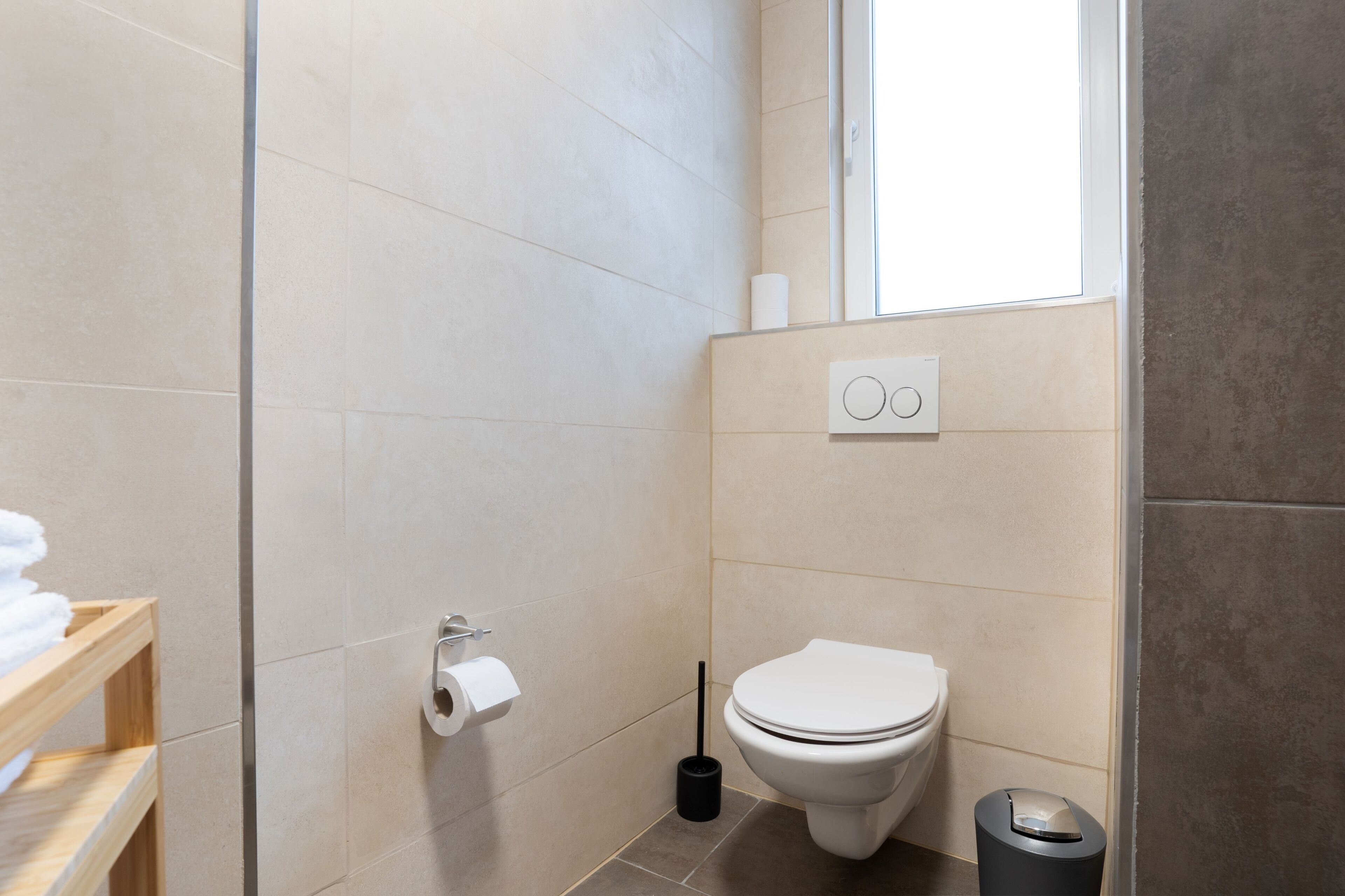 A modern bathroom with a toilet, a toilet paper holder, a bidet, and a trash bin.