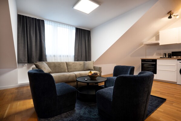 A modern living room with a sofa, two armchairs, a coffee table, and a kitchen area with a stove and cabinets.