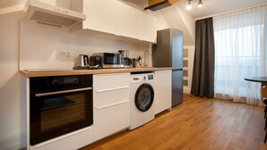 A compact kitchen with a built-in oven, microwave, and washing machine, wooden flooring, and a window with curtains. - Schöne Apartments in Bad Honnef (Bad Honnef)