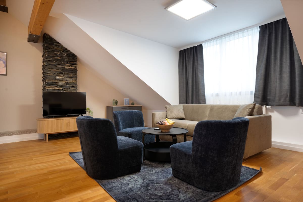 A modern living room with a stone accent wall, a flat-screen TV, a sofa, and two armchairs.
