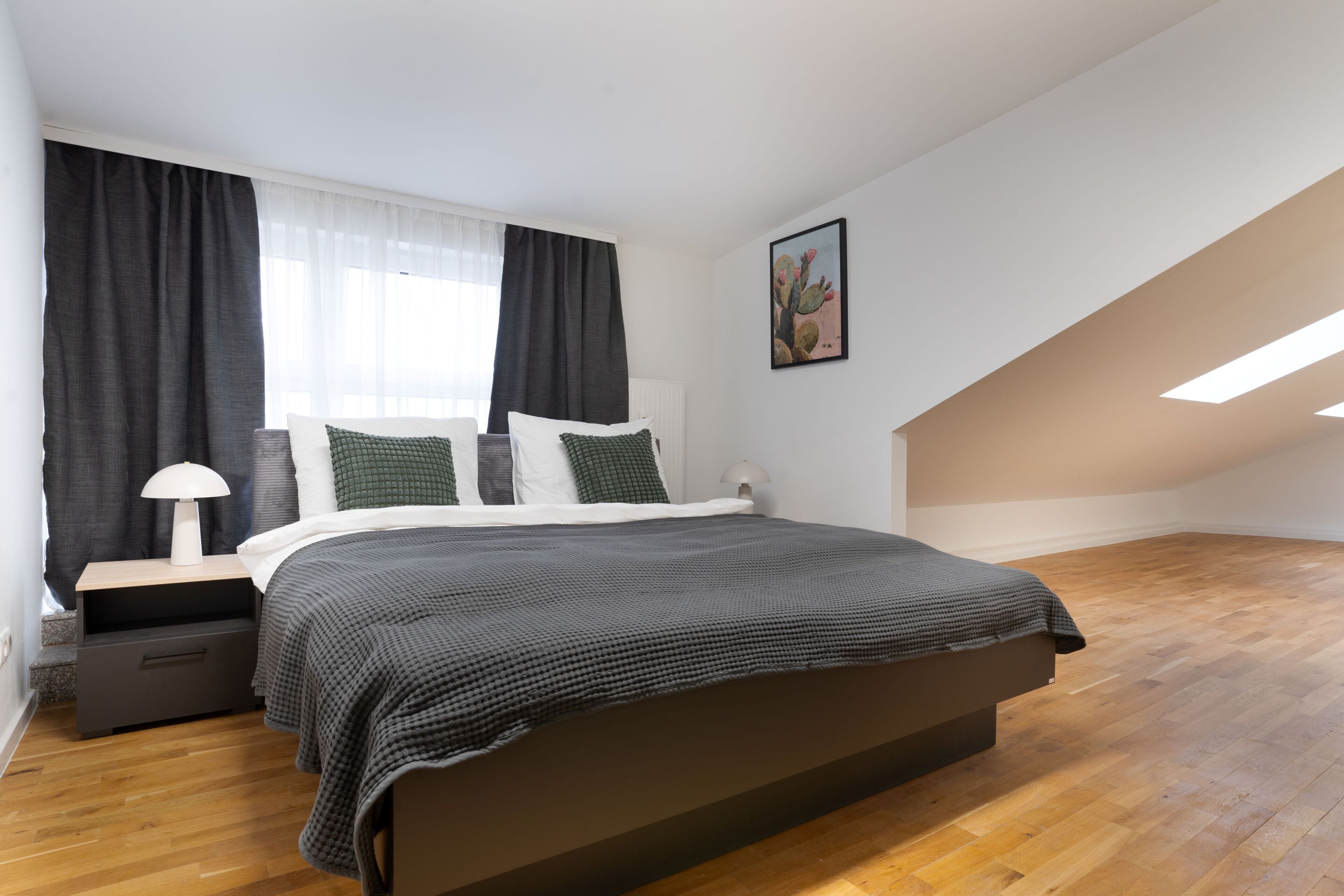 Une chambre à coucher avec un lit, une table de chevet, une lampe et une fenêtre avec des rideaux.