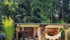 A wooden cabin with a patio, a hammock, and a grill area.