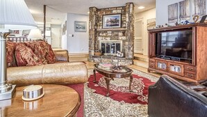 A living room with a stone fireplace, leather sofa, and a television stand. - 13419 - 19 Aldaya Lane (Hot Springs)