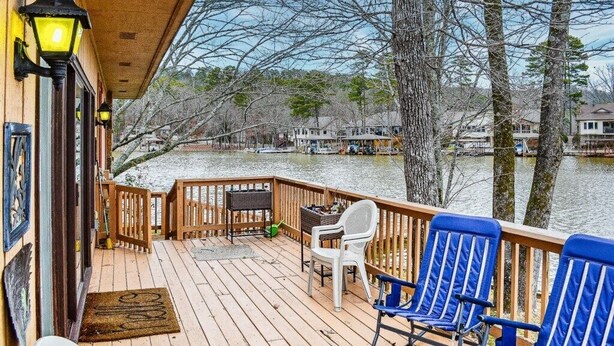 A wooden deck with blue chairs and a small table, overlooking a river with houses in the background. - 13419 - 19 Aldaya Lane (Hot Springs)